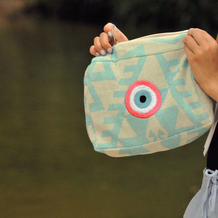 Hand Holding an Turquoise Cosmetic Pouch with Pink Evil Eye Embroidery 