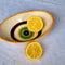 Casa Duniya's Hand-Painted Oval Yellow Evil Eye Bowls with Lemons against a White Linen Background