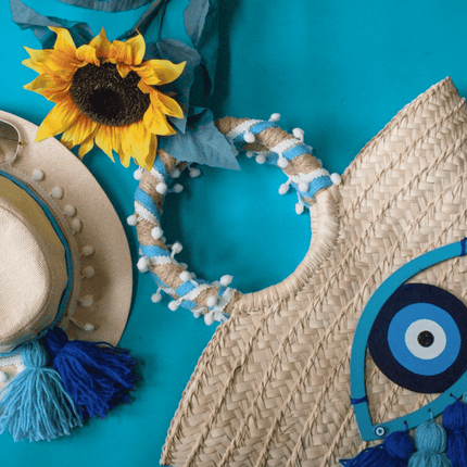 Casa Duniya's Hand Embroidered Evil Eye Beach Bag and Hat on a Turquoise Background with a sunflower as decor